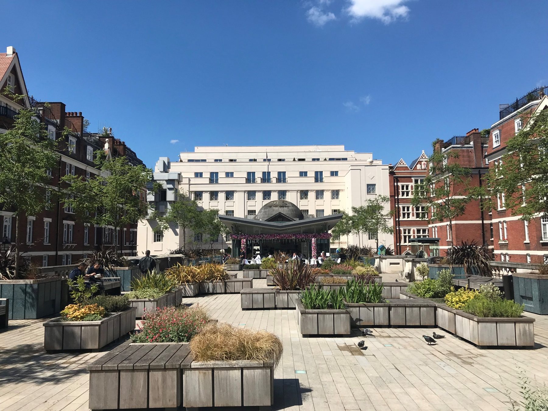 The Beaumont's white Art Deco façade seen across the planted terrace of Brown Hart Gardens, Mayfair, under a blue sky